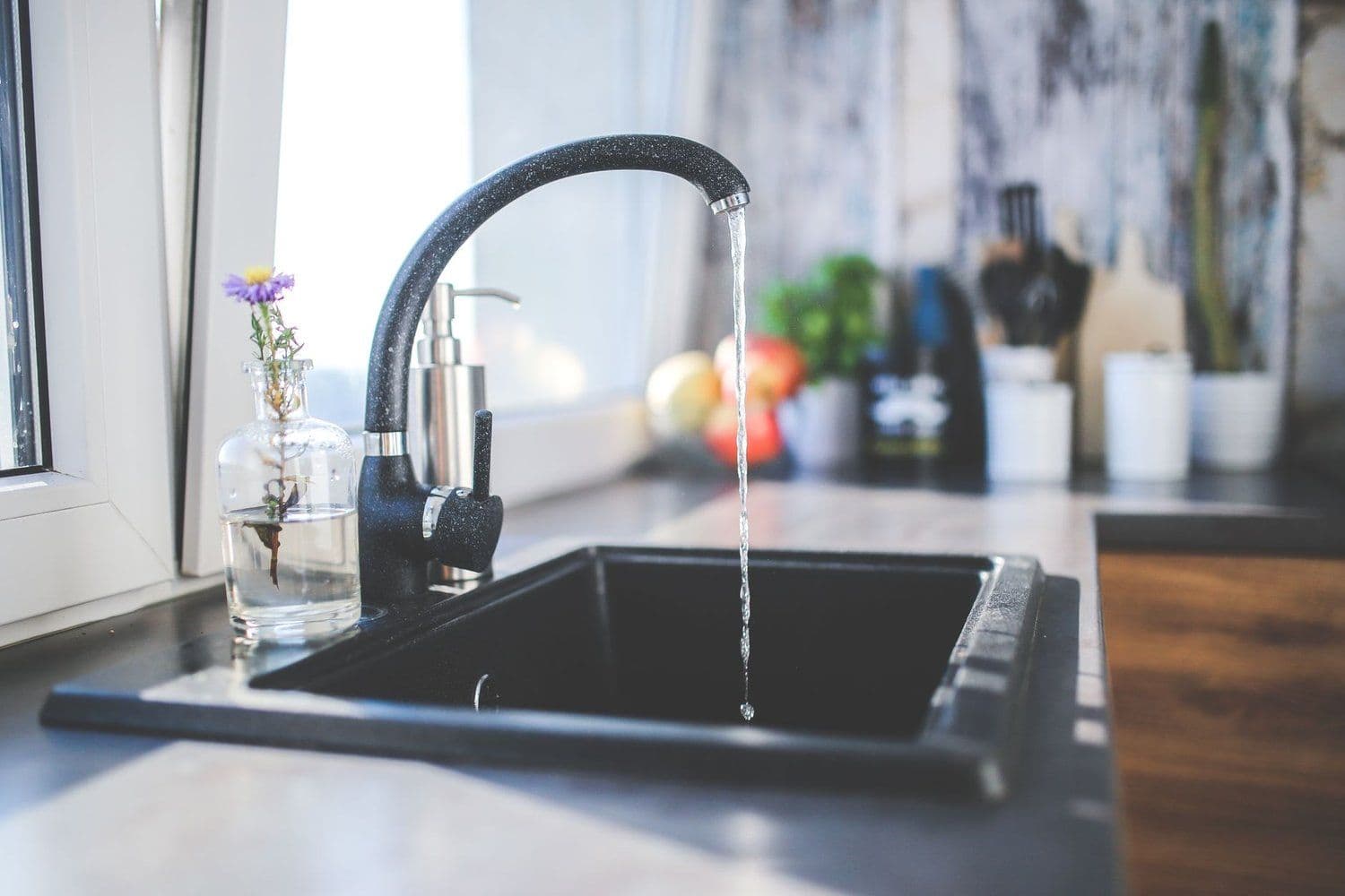 Water running from a black kitchen faucet into a dark sink