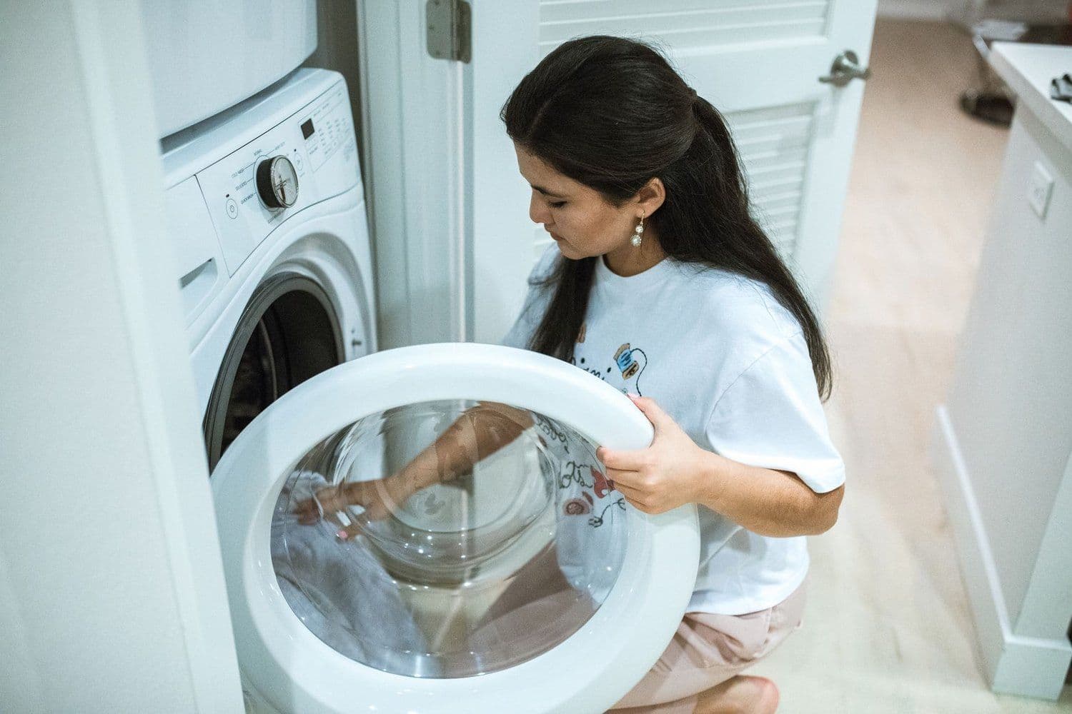 Woman wiping the door seal of an open front-loading washer in a home laundry room