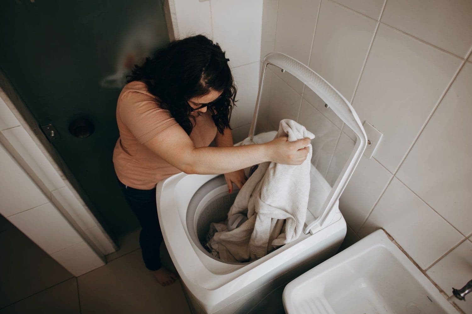 Woman lifting laundry out of a white top-loading washing machine